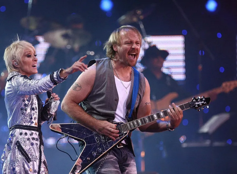 Alfredo Alonso tocando una guitarra Flying V en vivo, junto a una cantante