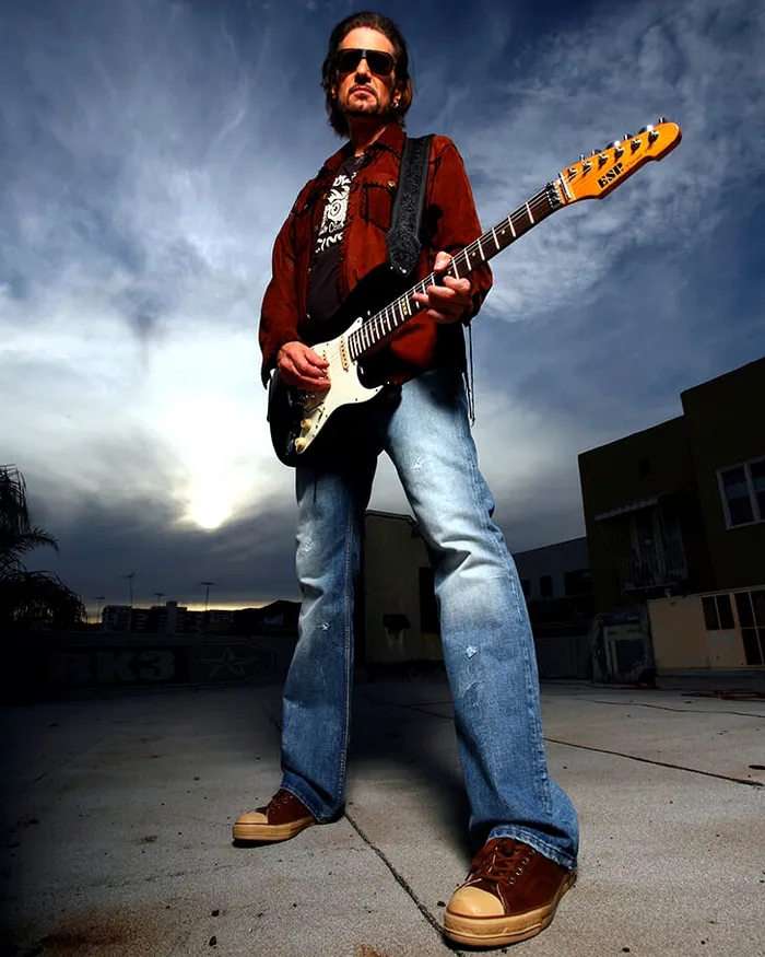Bruce Kulick tocando una guitarra Stratocaster en una azotea, al atardecer