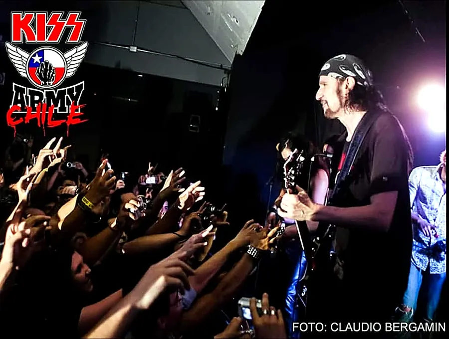 Bruce Kulick tocando la guitarra frente al público con las manos en alto, en el Club 334