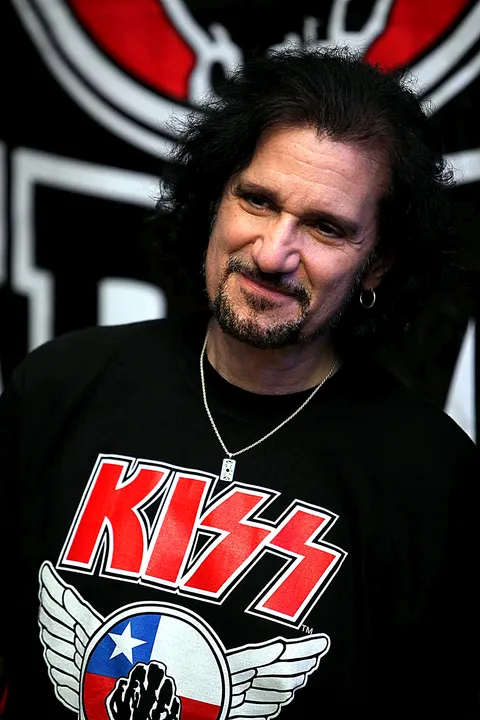 Retrato de Bruce Kulick sonriendo, con una polera de KISS Army Chile