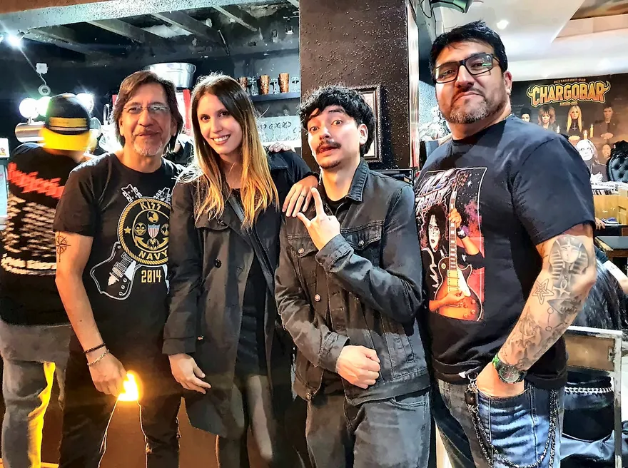 Cuatro asistentes posando en Chargobar, uno con una polera de Ace Frehley con su guitarra