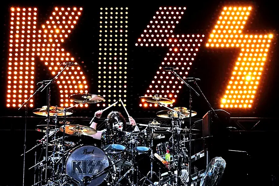 Eric Singer tocando la batería frente al letrero luminoso de KISS