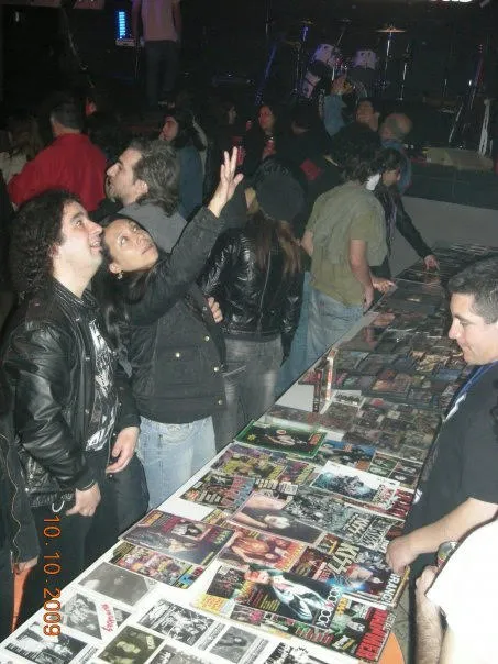 Fans de KISS Army Chile mirando la mesa de exhibición, uno de ellos saludando hacia el escenario