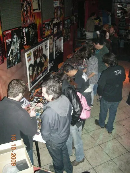 Fans revisando la colección de revistas y memorabilia kissera sobre la mesa de exhibición
