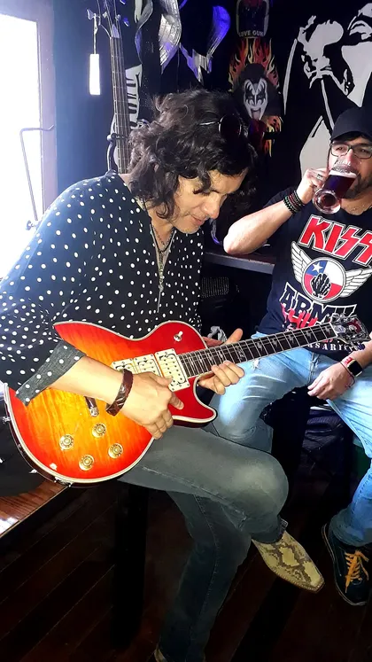 Fan tocando la guitarra en el Kiss Day, con otro fan disfrutando de una cerveza