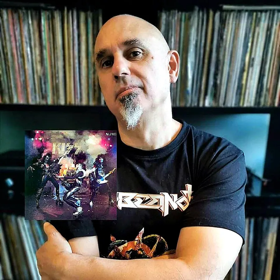 Rolando Ramos mostrando la portada de Alive! de KISS frente a su colección de vinilos